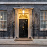 The office of the UK's Prime Minister. A black front door with the number 10 on it, with windows either side and. and lit with a lamp overhead.